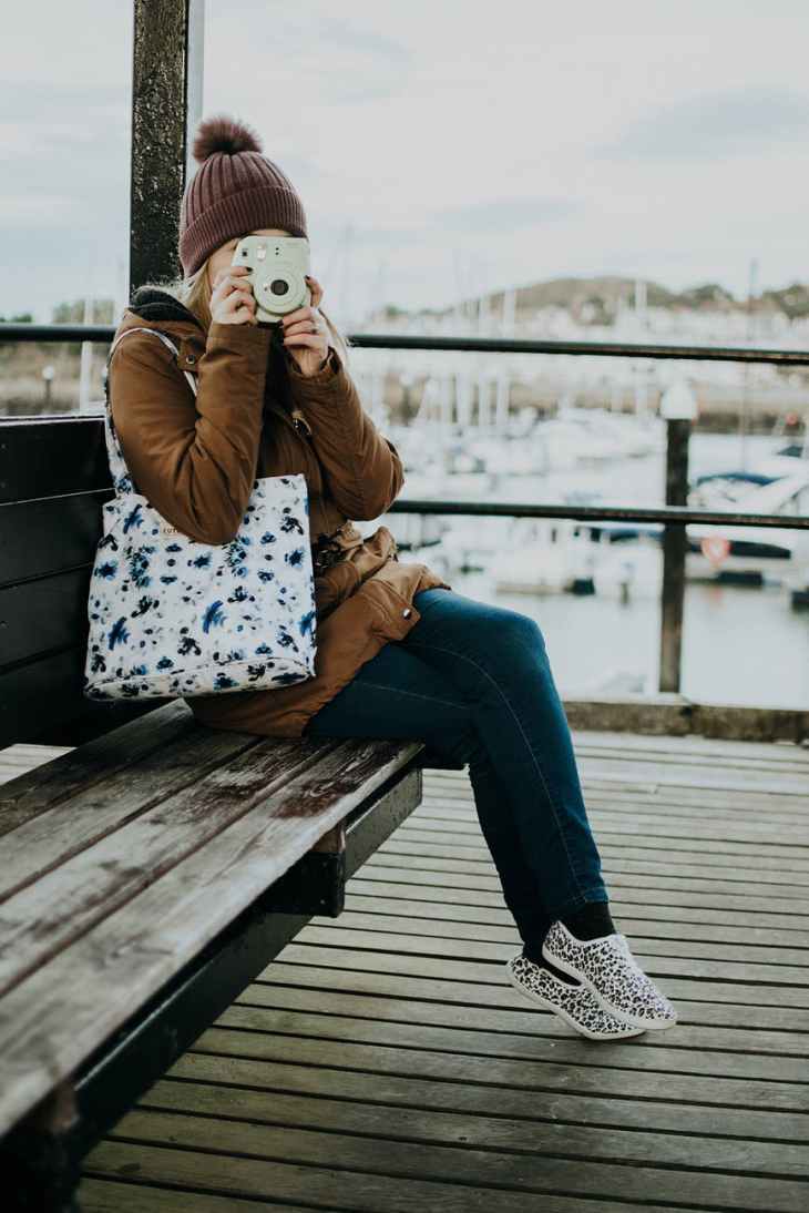 woman taking picture while sitting on wooden bench